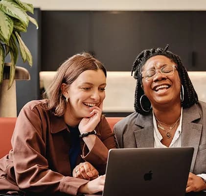 Two colleagues laughing together while looking at a laptop