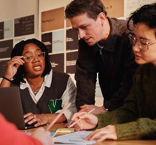 Three colleagues reviewing notes together around a laptop