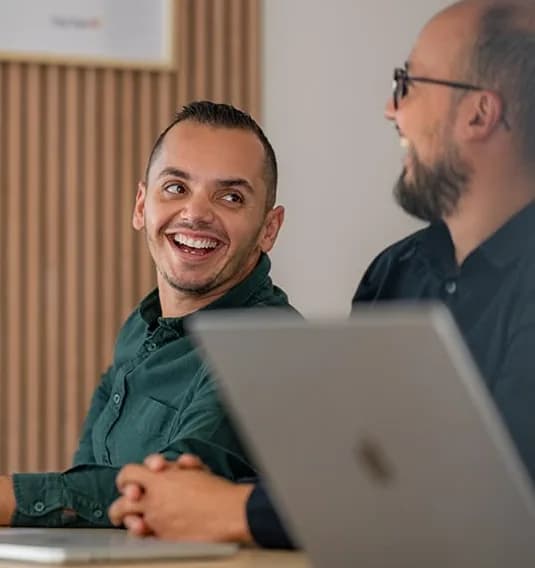 Two colleagues laughing together beside a laptop
