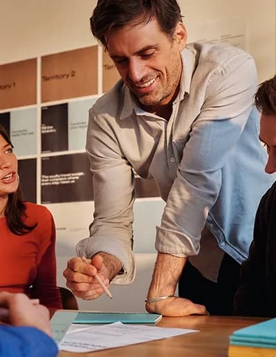 Smiling colleague leaning over a table to annotate notes during a workshop