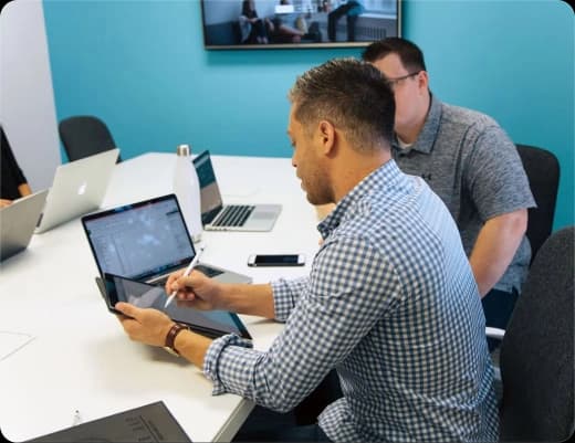 Two analysts reviewing research on a tablet in a meeting room