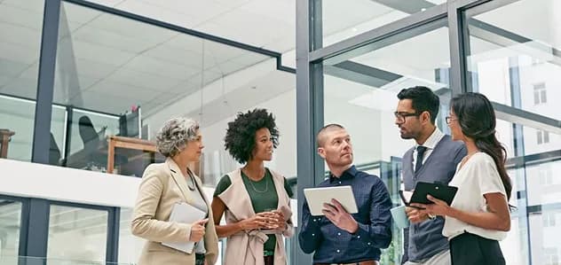 A group of colleagues talking with tablets in a glass-walled office