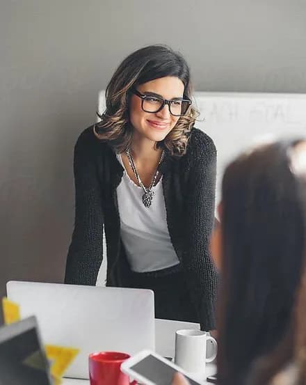 A smiling professional leaning over a desk in a meeting