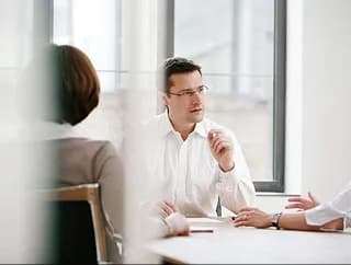 A professional speaking with colleagues across a bright meeting table