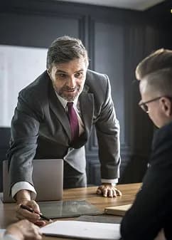 A senior professional leaning over a table to talk with a colleague