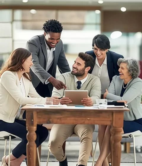 A smiling team gathered around a tablet at a wooden table