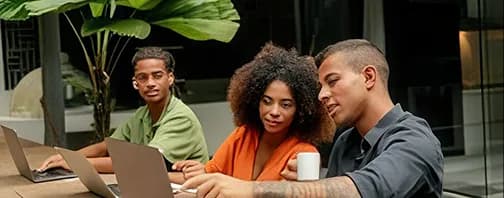 Three colleagues reviewing work on a laptop at an outdoor table