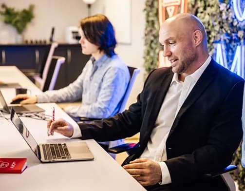 Two colleagues working on laptops at a shared office desk