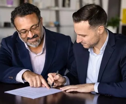 Two colleagues reviewing and signing a document at a desk