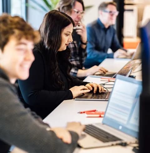 Colleagues working on laptops along a shared office desk