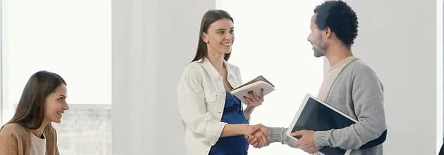 Two people shaking hands in a bright office while a colleague looks on