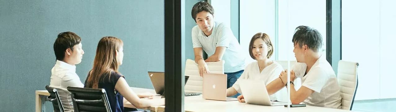 Colleagues working with laptops around a table in a glass-walled office