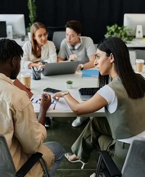 Colleagues discussing printouts and laptops around a meeting table