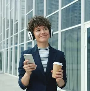 Person walking outdoors with headphones, a phone and a coffee cup