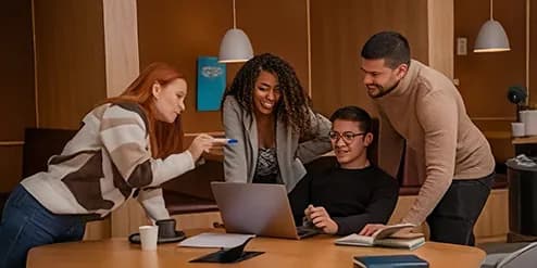 Four colleagues gathered around a laptop in a lounge area