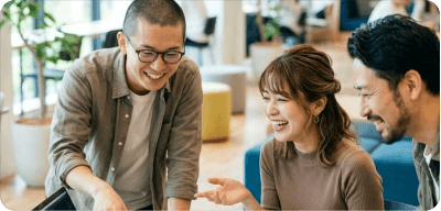 Three professionals smiling and collaborating together around a desk workspace