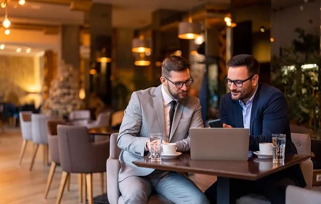 Two colleagues working on a laptop at a cafe table