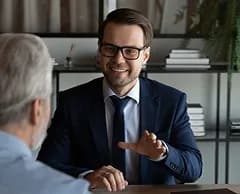 A smiling adviser in glasses talking with a client across a desk