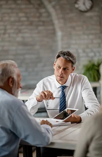 An adviser holding a tablet listening to an older client across a table