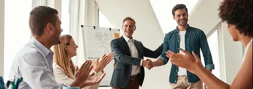 Colleagues applauding as two teammates shake hands in a meeting room