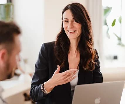 A support specialist smiling while explaining something beside a laptop
