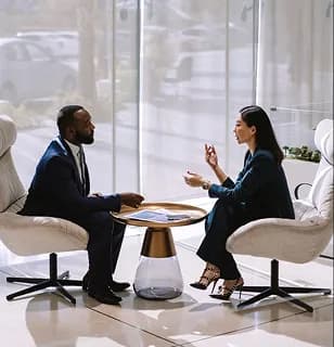 Two professionals in conversation across a small lounge table