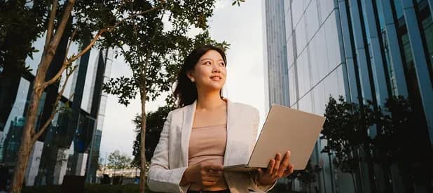 A professional holding a laptop outside modern office towers