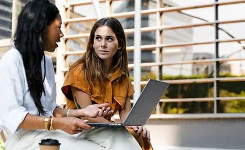 Two colleagues discussing work on a laptop outdoors