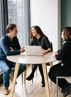 Three colleagues talking around a laptop at a small table