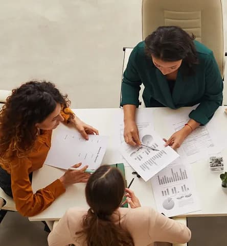 Overhead view of three colleagues reviewing printed charts at a desk