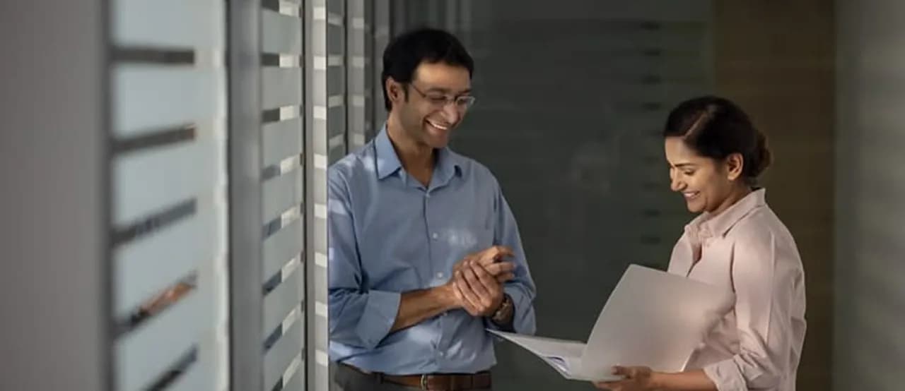 Two colleagues smiling while reviewing a document in a hallway