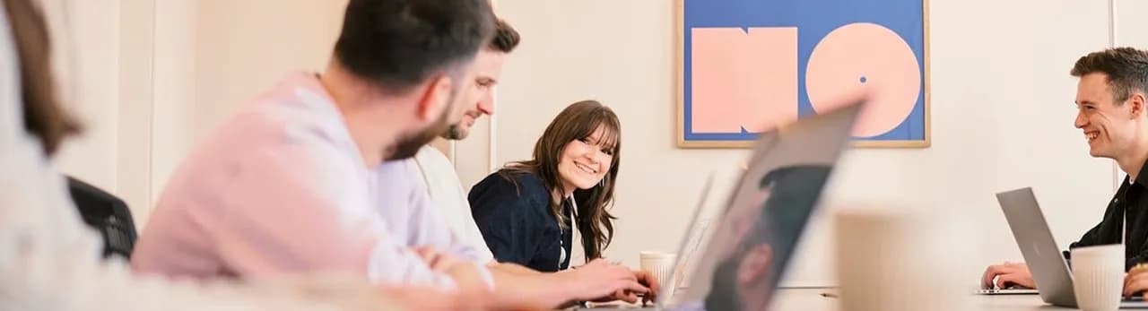 Colleagues smiling while working on laptops around a table