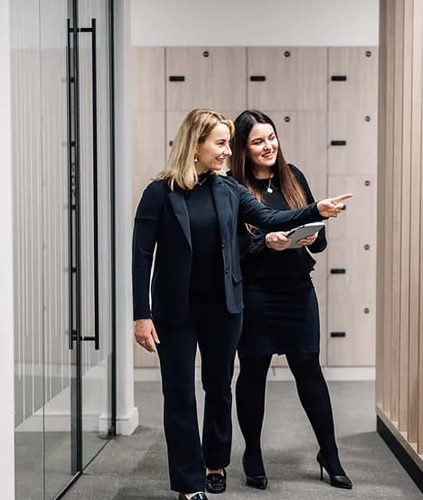 Two colleagues walking down an office corridor, one pointing ahead