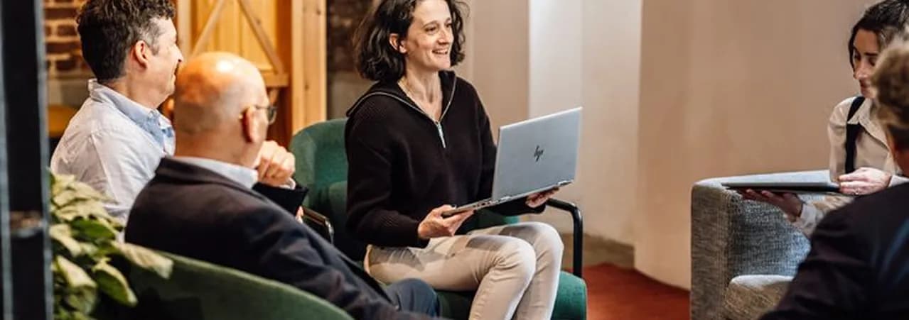 A woman with a laptop leading a relaxed discussion with colleagues