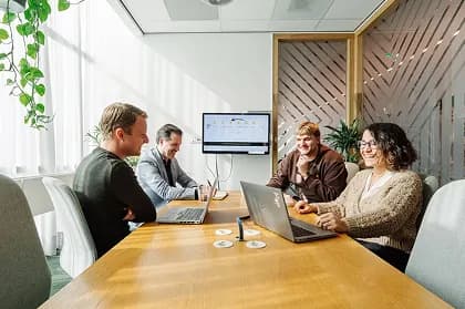 Colleagues laughing around a meeting-room table with laptops